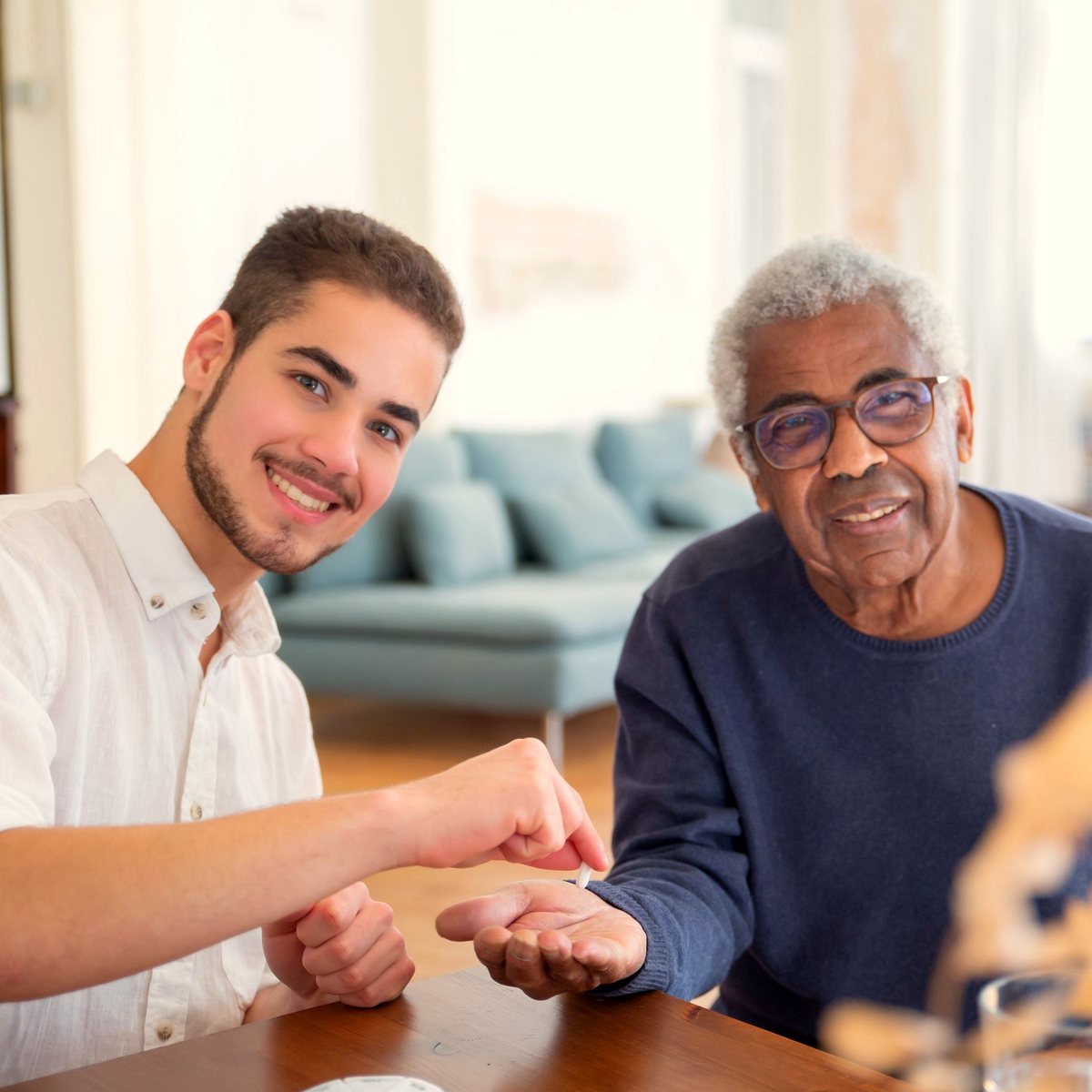 Care worker placing a tablet into a client's hand at the kitchen table