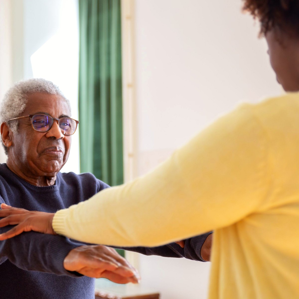 Care worker supporting an older man with seated arm exercises at home
